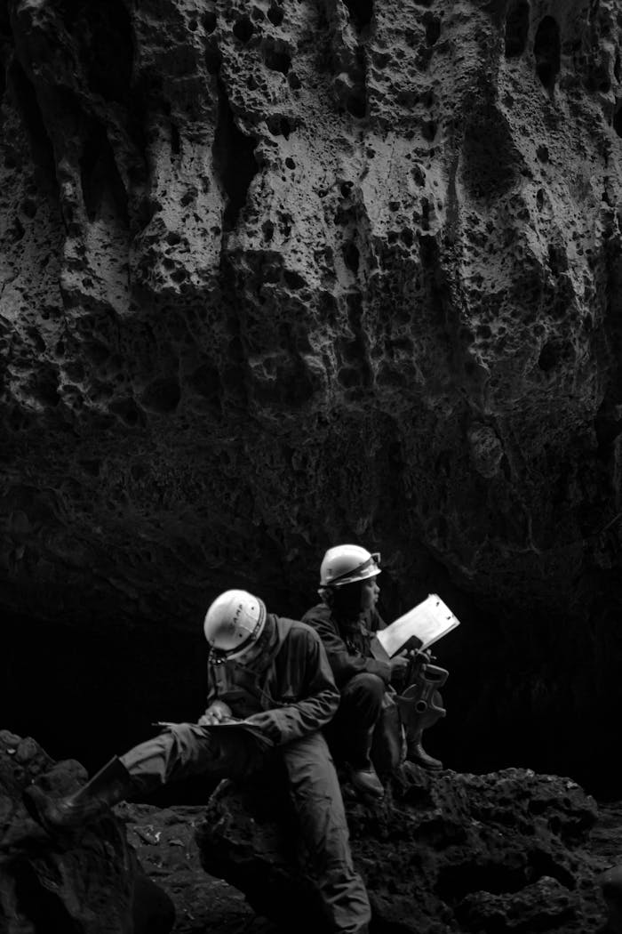 Grayscale Photo of Men Wearing Helmets in a Cave